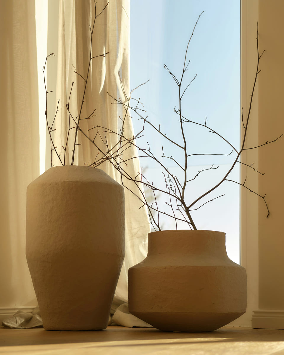 Two textured clay vases with bare branches in warm window light.