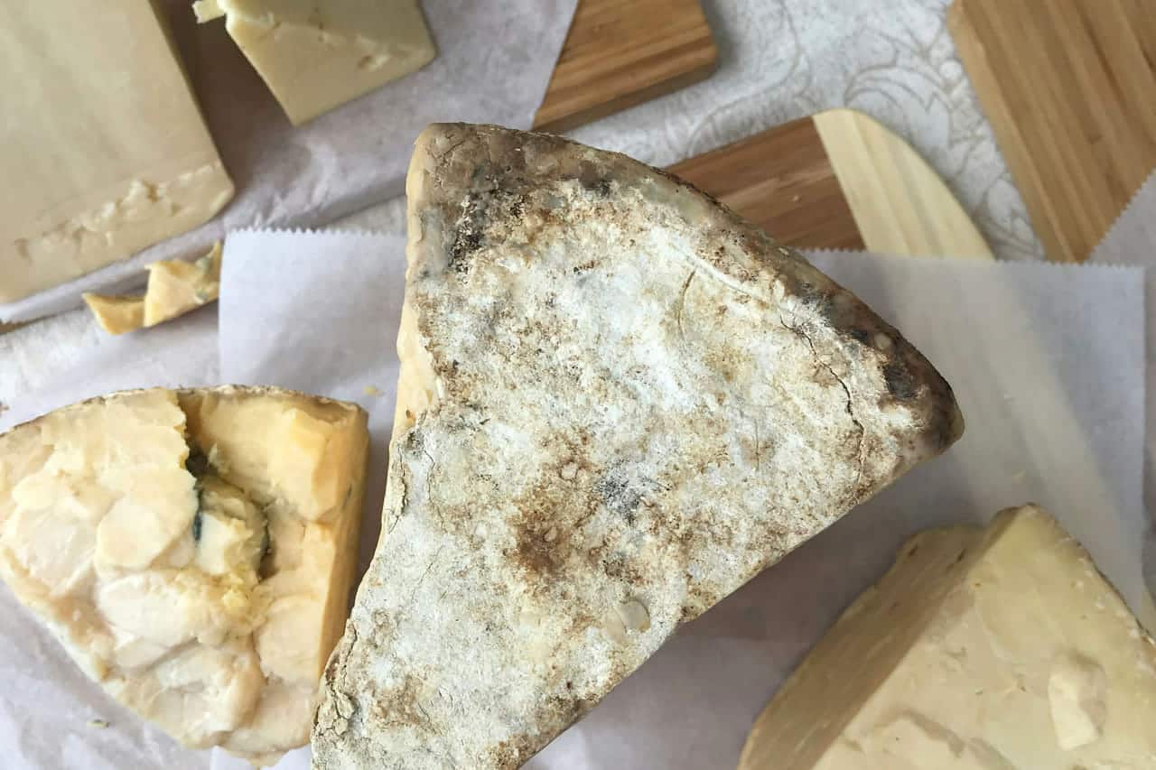 Wedges of blue and firm cheese unwrapped on white cheese paper on a wooden table.