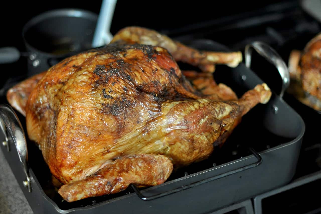 A golden-brown roast turkey in a dark roasting pan on the stovetop.